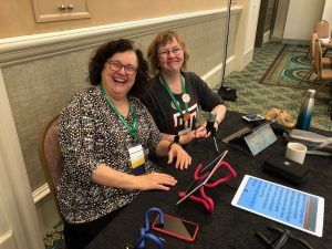 Image of Kathryn and Kim sitting at a table with an iPad mounted on an industrial twist tie.