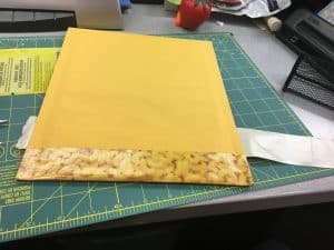 Image of a padded mailer being covered in duct tape.