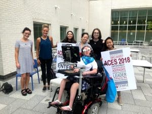 Image of AAC user in wheelchair surrounded by ACES volunteers and rocking awesome sunglasses.