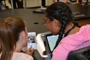 TWo young women, one with an AAC device, looking at a selfie.